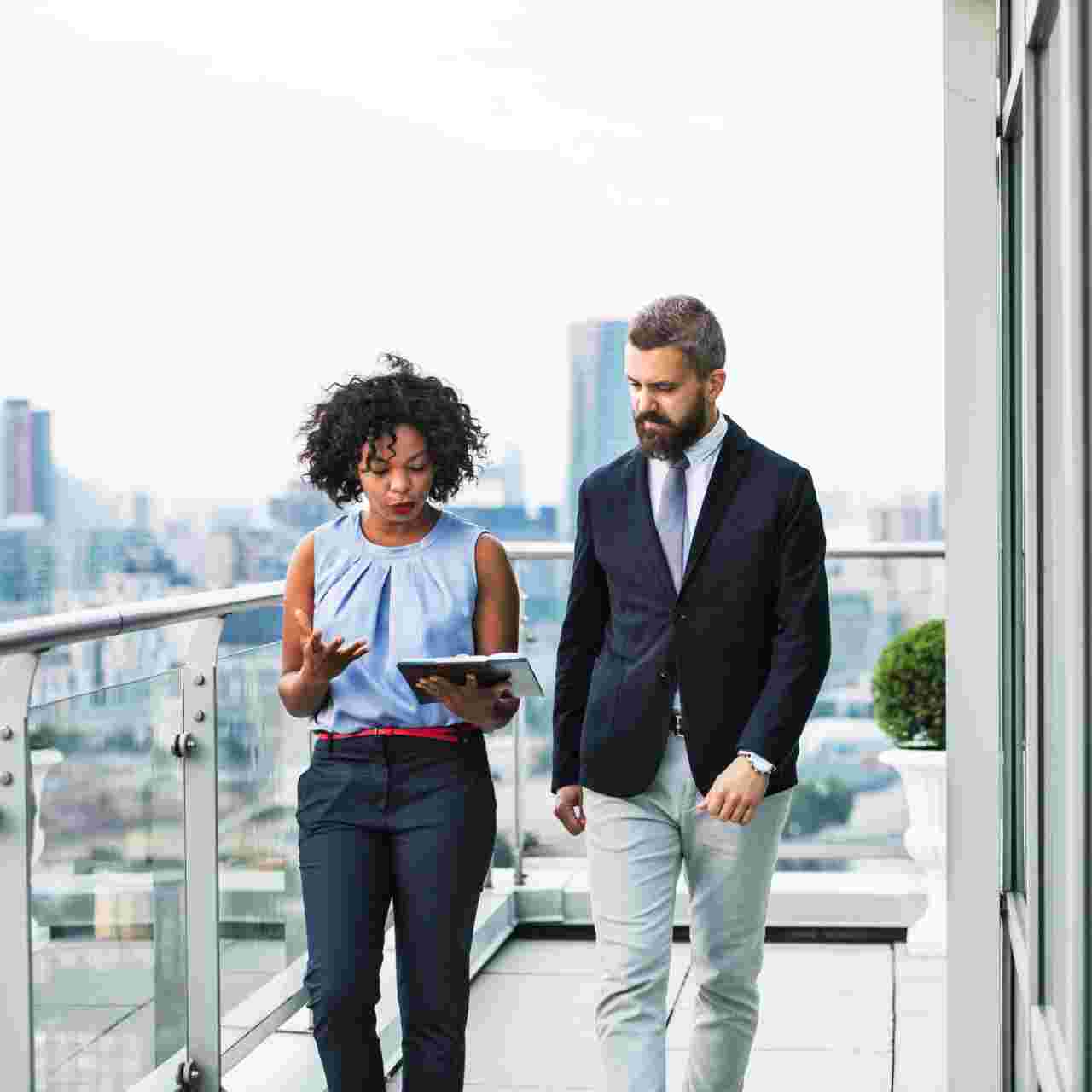 A portrait of businesspeople walking against London rooftop view, discussing something.